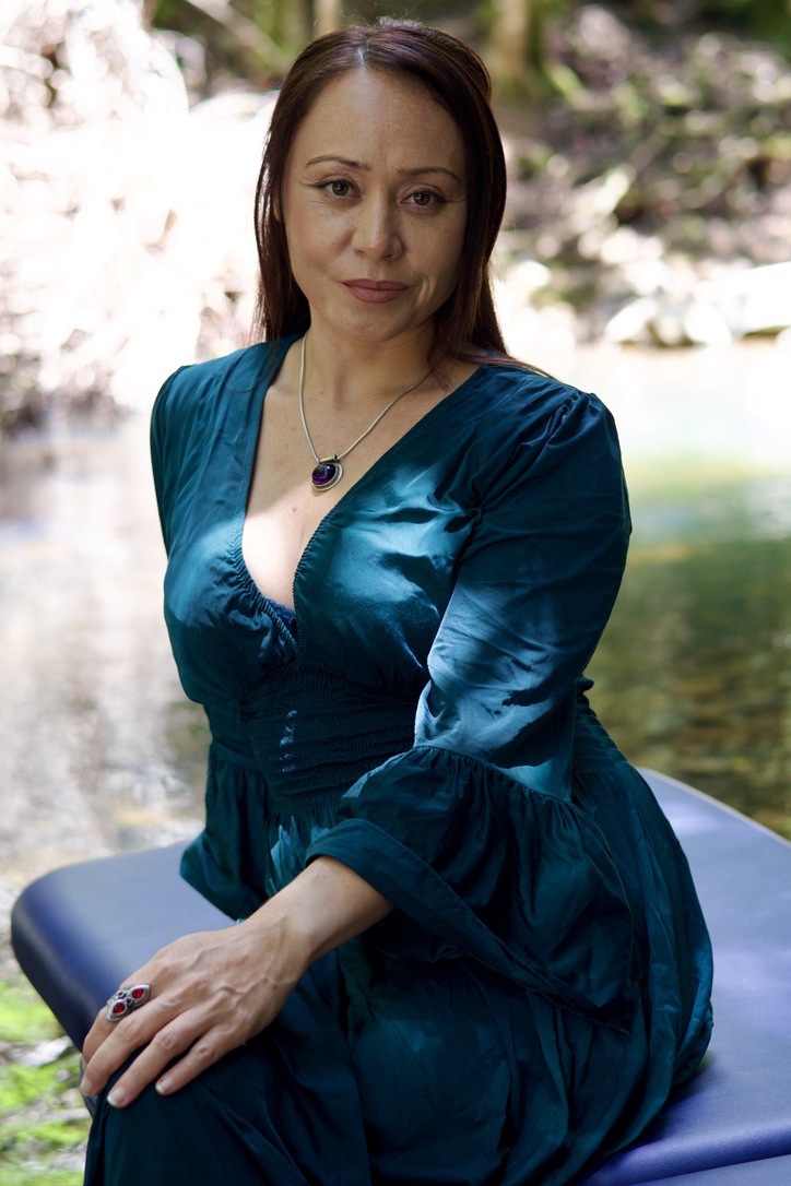 Woman in teal dress sitting by a serene river.